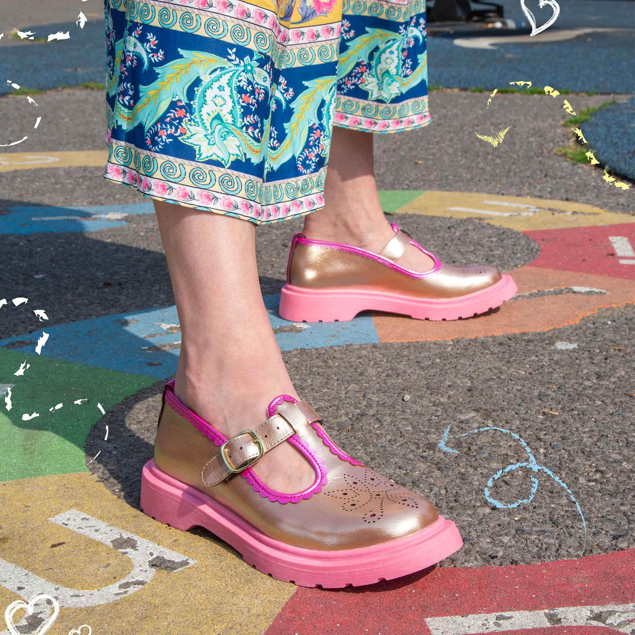 Person wearing metallic pink and gold T Bar shoes on a colourful playground surface